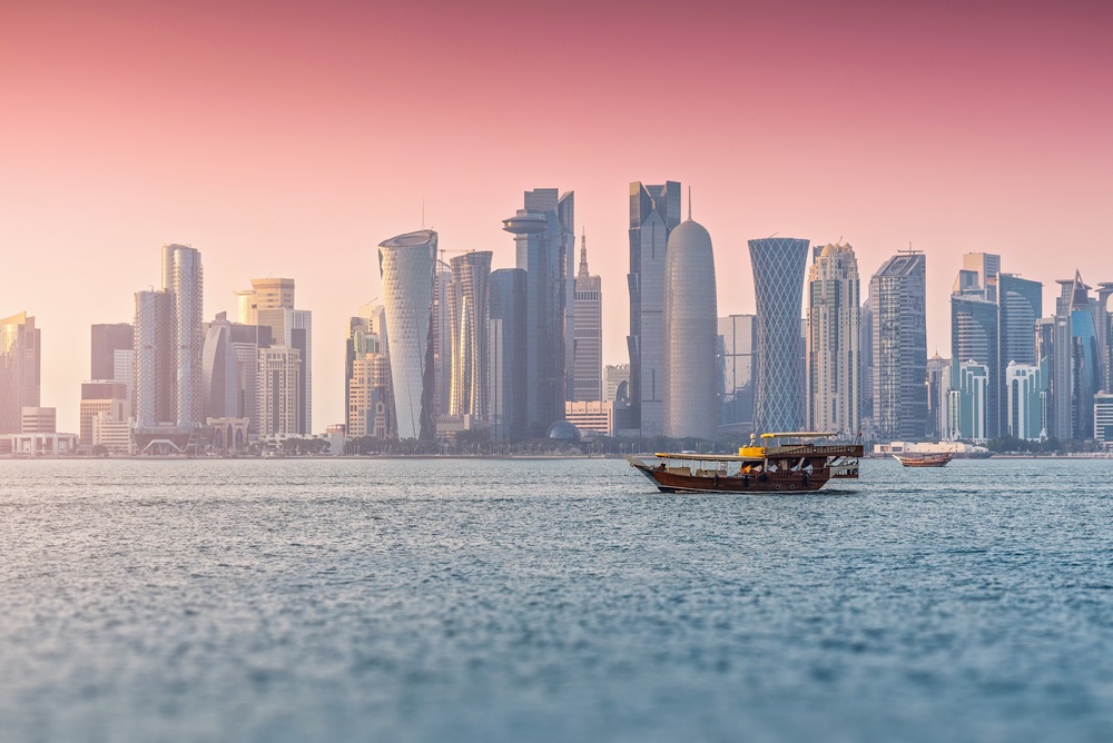 Doha skyline at sunset with traditional dhow boat on the water