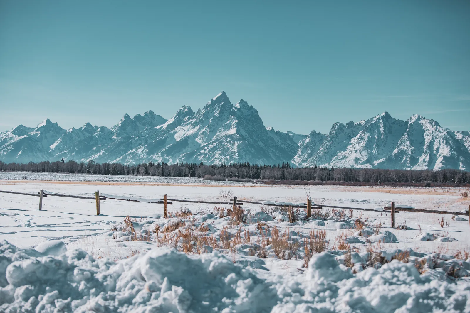 Snow-covered Teton Range above a snowy meadow and wooden fence near Jackson Hole in winter